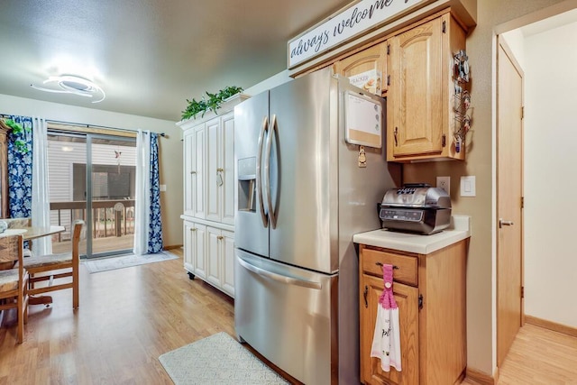 kitchen featuring baseboards, light countertops, light wood finished floors, and stainless steel fridge with ice dispenser