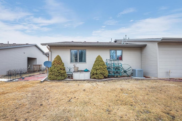 rear view of property featuring central air condition unit, fence, and a lawn