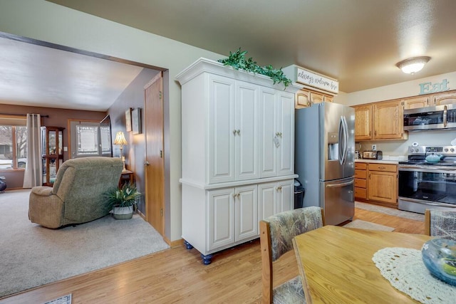 kitchen with light wood finished floors, stainless steel appliances, light countertops, and open floor plan