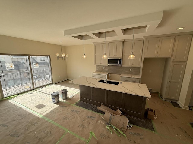 kitchen with a sink, backsplash, light stone countertops, stainless steel microwave, and decorative light fixtures