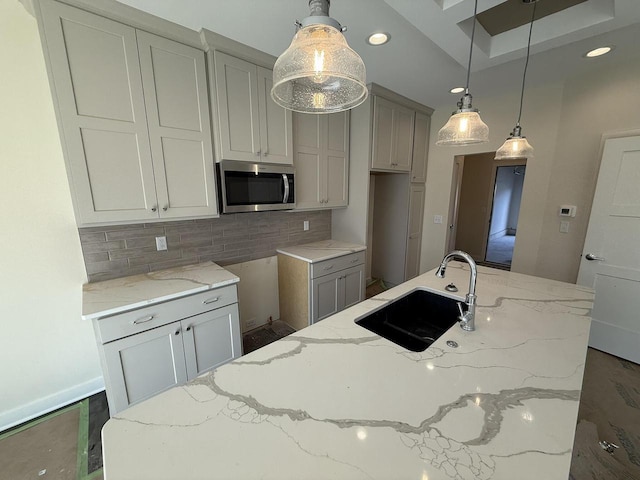 kitchen featuring tasteful backsplash, stainless steel microwave, a sink, and light stone counters