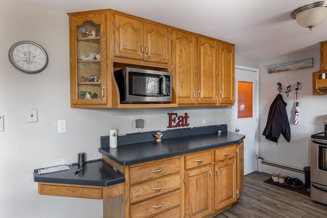 kitchen featuring dark wood-style flooring, brown cabinets, dark countertops, appliances with stainless steel finishes, and glass insert cabinets