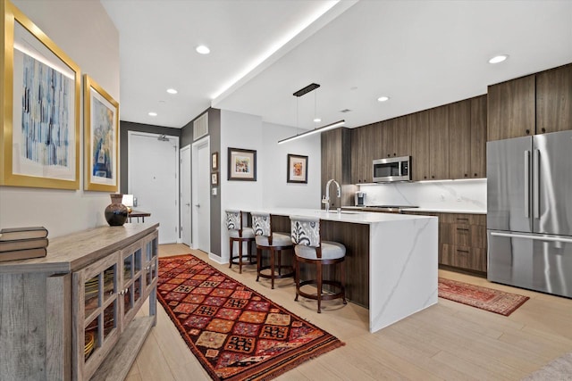 kitchen with a sink, a kitchen breakfast bar, appliances with stainless steel finishes, modern cabinets, and a center island with sink