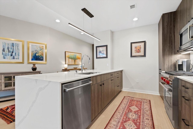 kitchen featuring stainless steel appliances, light wood-style floors, a sink, modern cabinets, and a peninsula