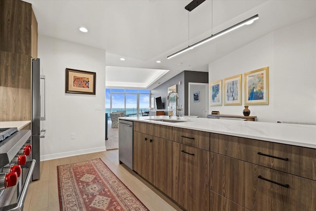 kitchen with light countertops, appliances with stainless steel finishes, a sink, modern cabinets, and light wood-type flooring