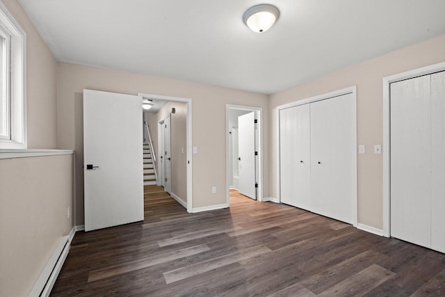 unfurnished bedroom featuring a baseboard heating unit, wood finished floors, two closets, and baseboards