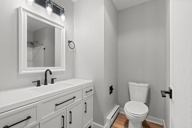 bathroom with toilet, baseboard heating, vanity, wood finished floors, and baseboards