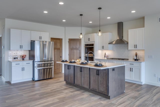 kitchen with light wood finished floors, white cabinets, stainless steel appliances, light countertops, and wall chimney range hood