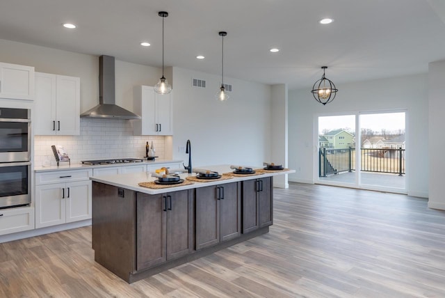 kitchen featuring white cabinetry, wall chimney exhaust hood, appliances with stainless steel finishes, and light countertops