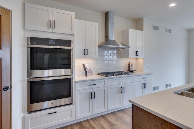 kitchen featuring stainless steel appliances, visible vents, white cabinetry, wall chimney range hood, and decorative backsplash