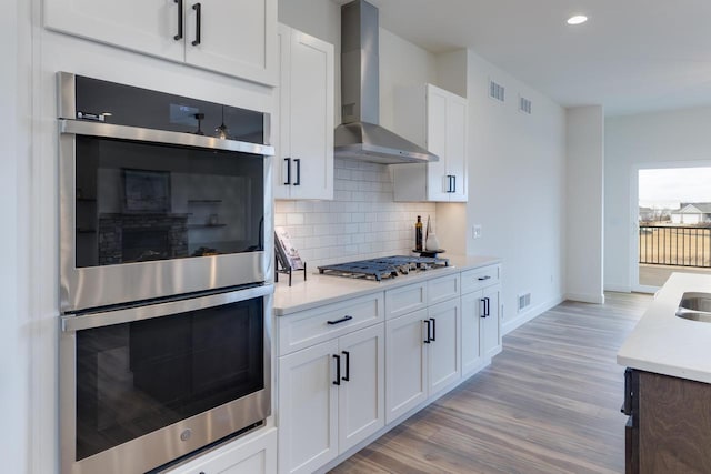 kitchen featuring visible vents, light countertops, decorative backsplash, appliances with stainless steel finishes, and wall chimney range hood