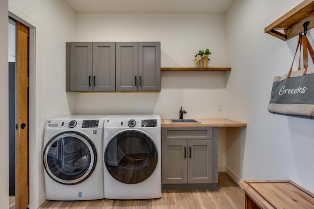 laundry area with cabinet space, baseboards, washing machine and clothes dryer, light wood-style floors, and a sink