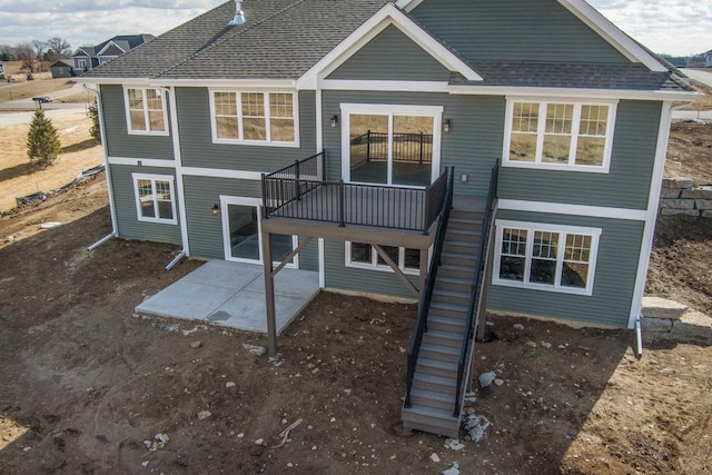 back of property featuring stairs, a deck, roof with shingles, and a patio area