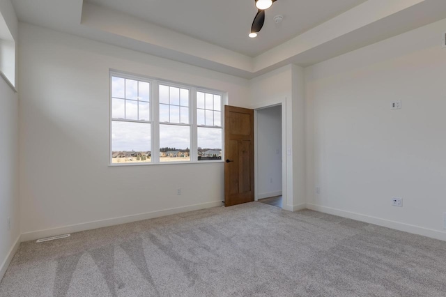 carpeted empty room with a tray ceiling, visible vents, ceiling fan, and baseboards