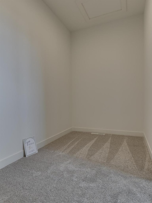 carpeted empty room with attic access and baseboards