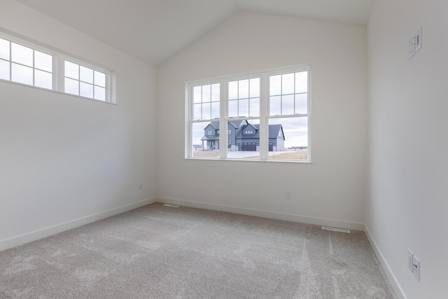 carpeted empty room with lofted ceiling, a healthy amount of sunlight, visible vents, and baseboards