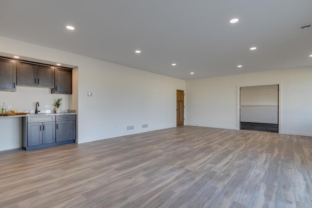 unfurnished living room with light wood-type flooring, wet bar, a sink, and recessed lighting