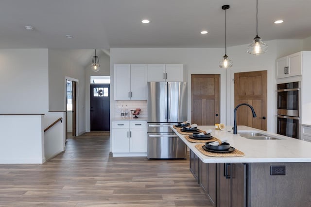 kitchen with light wood finished floors, white cabinets, appliances with stainless steel finishes, a sink, and backsplash