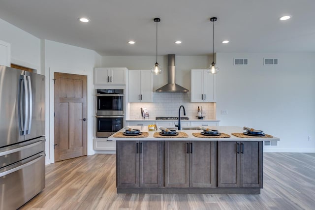 kitchen featuring light countertops, visible vents, appliances with stainless steel finishes, white cabinets, and wall chimney range hood