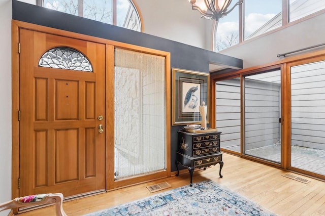 foyer with an inviting chandelier, visible vents, a high ceiling, and wood finished floors