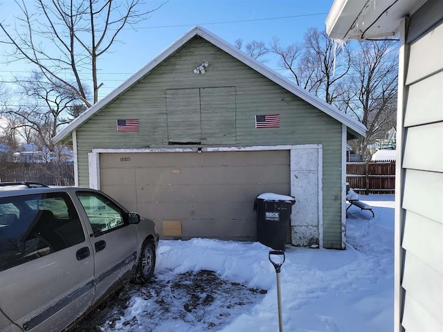 snow covered garage featuring fence and a detached garage