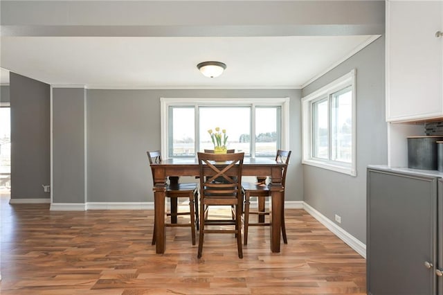 dining area with baseboards, crown molding, and light wood finished floors