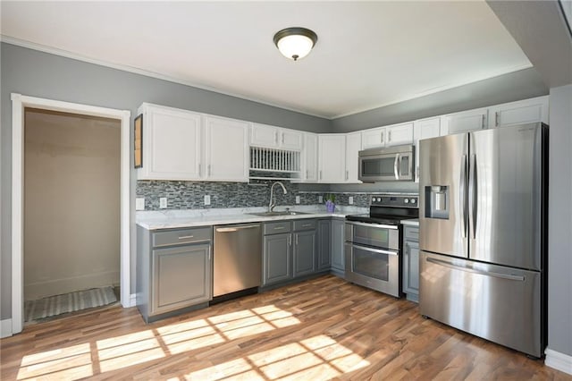 kitchen with light countertops, gray cabinetry, appliances with stainless steel finishes, light wood-style floors, and a sink