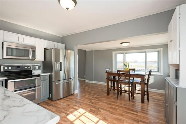 kitchen with white cabinets, light stone counters, stainless steel appliances, crown molding, and light wood-type flooring