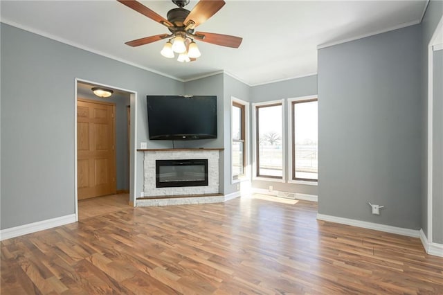 unfurnished living room with crown molding, ceiling fan, a stone fireplace, wood finished floors, and baseboards