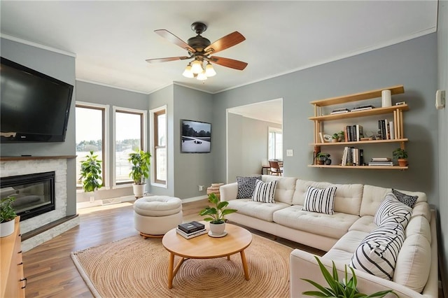 living room featuring a fireplace, ornamental molding, ceiling fan, wood finished floors, and baseboards