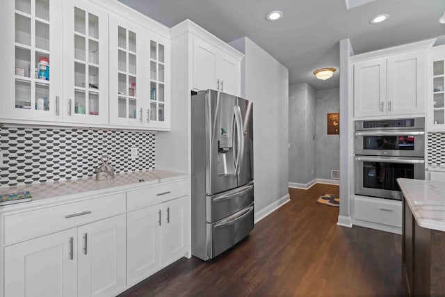 kitchen featuring tasteful backsplash, glass insert cabinets, appliances with stainless steel finishes, dark wood-style floors, and white cabinetry