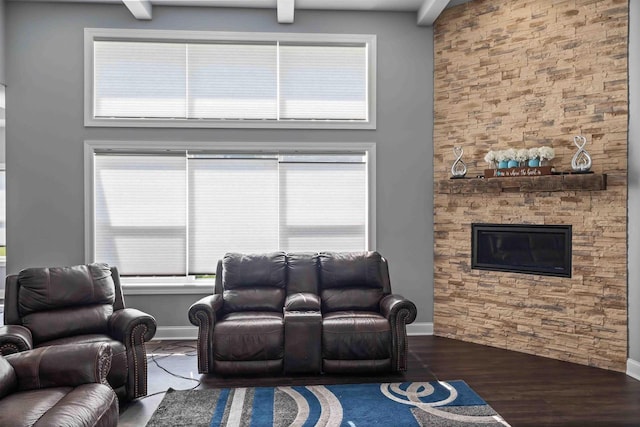 living area with a stone fireplace, wood finished floors, baseboards, and a towering ceiling