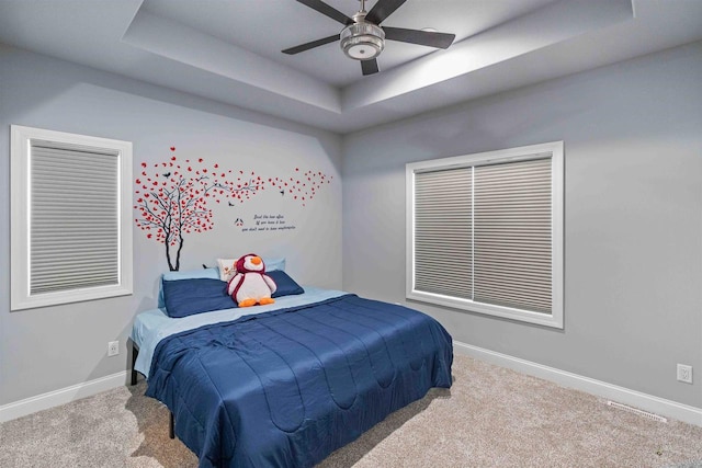 carpeted bedroom with a ceiling fan, a raised ceiling, and baseboards