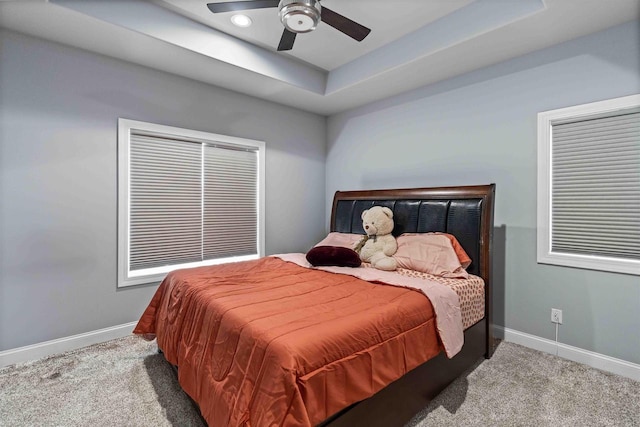 carpeted bedroom with a raised ceiling, baseboards, and ceiling fan