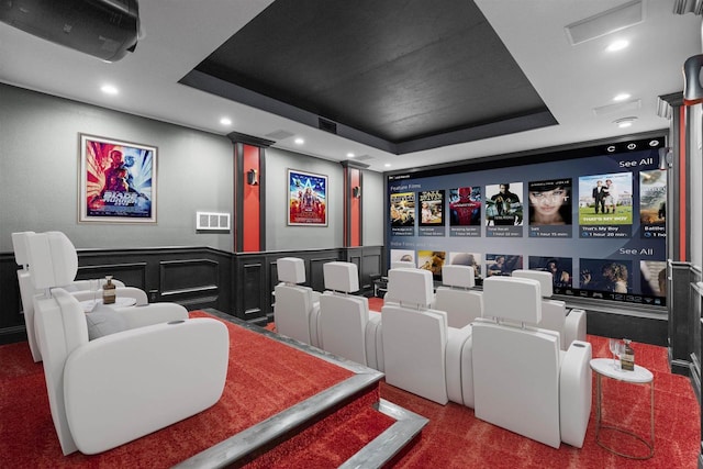 carpeted cinema room with a raised ceiling, a decorative wall, and recessed lighting