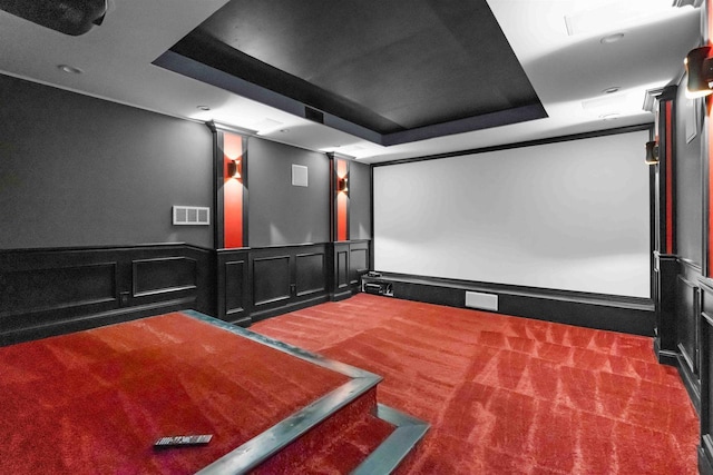 home theater room featuring wainscoting, visible vents, carpet flooring, and a raised ceiling