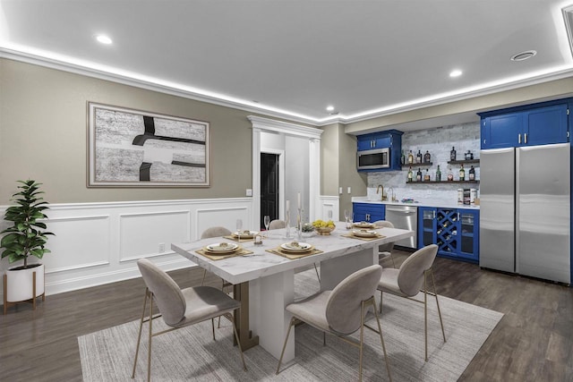 dining room with recessed lighting, wet bar, dark wood finished floors, and a decorative wall