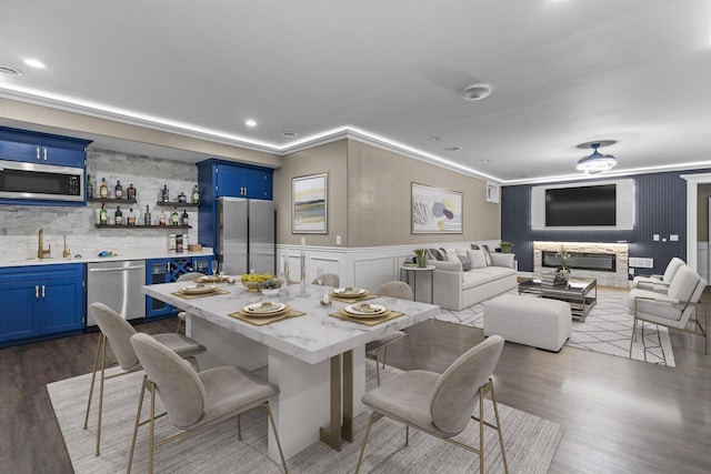 dining space with indoor wet bar, a stone fireplace, crown molding, and dark wood-type flooring