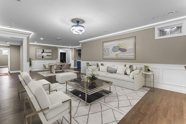 living room featuring recessed lighting, a decorative wall, ornamental molding, and wood finished floors