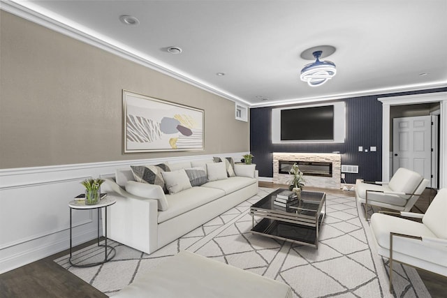 living area featuring visible vents, crown molding, a wainscoted wall, a stone fireplace, and wood finished floors