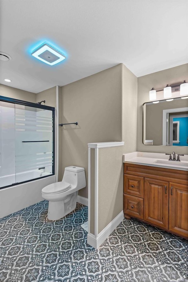 bathroom featuring tile patterned floors, toilet, shower / bath combination with glass door, baseboards, and vanity