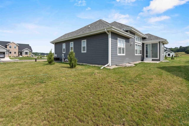 back of house featuring a lawn and roof with shingles