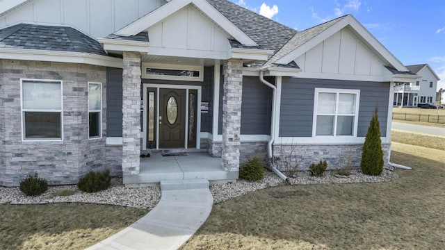 doorway to property featuring board and batten siding, stone siding, and a shingled roof