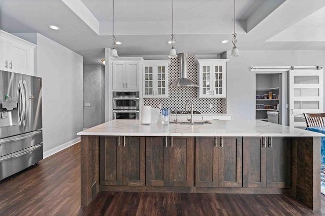 kitchen featuring dark wood-type flooring, wall chimney range hood, a barn door, stainless steel appliances, and a raised ceiling