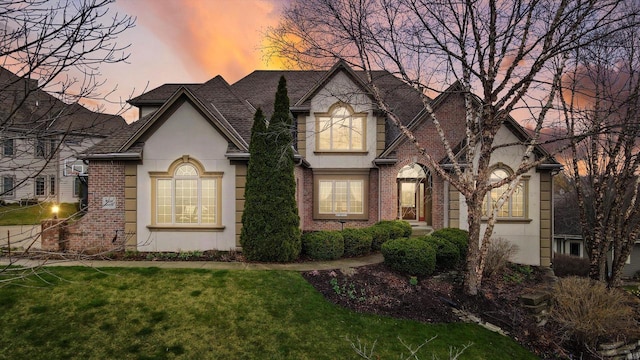 view of front facade with brick siding, a front lawn, and stucco siding