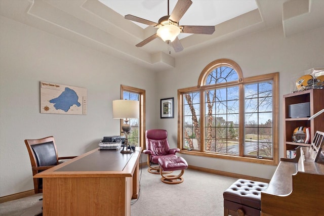 carpeted office space featuring baseboards, a tray ceiling, and ceiling fan