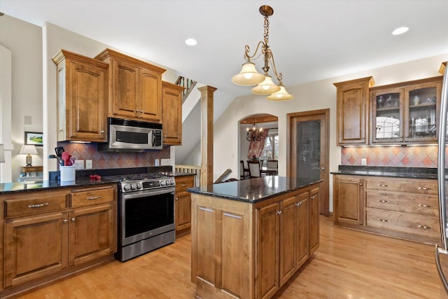 kitchen with arched walkways, light wood-style flooring, stainless steel appliances, a kitchen island, and brown cabinetry