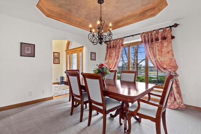 carpeted dining room featuring a tray ceiling, a notable chandelier, arched walkways, and baseboards