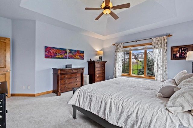 carpeted bedroom featuring a raised ceiling, a ceiling fan, and baseboards