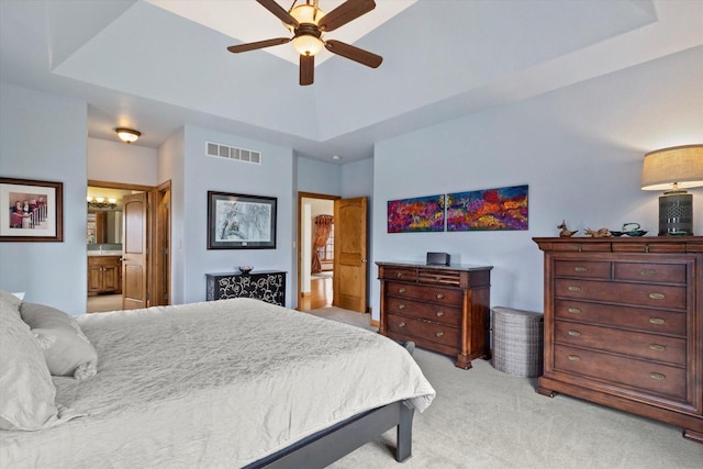 bedroom featuring light colored carpet, a ceiling fan, visible vents, a tray ceiling, and ensuite bath